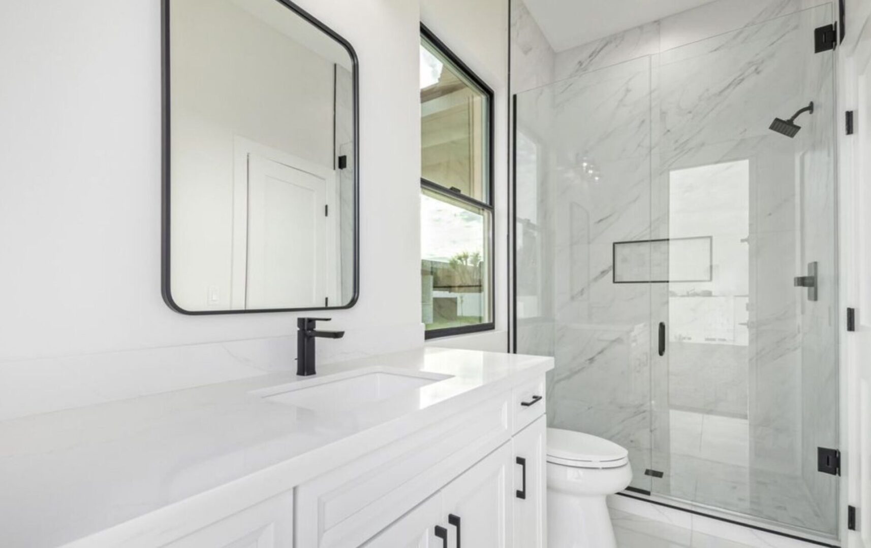 A bathroom with white cabinets and black framed mirror.